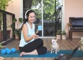 Asian woman wearing headphones, holding coffee cup, using smartphone, sitting  on yoga mat in balcony  with computer laptop Royalty Free Stock Photo