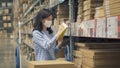 Asian woman wearing a mask working or shopping on shelves at large warehouse retail store industry. Rack of furniture and home