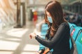 Asian woman wearing medical protective face mask looking at her wrist watch for checking time in terminal lounge at airport,