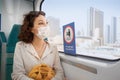 Woman wearing a protective face mask sits on a subway seat and looks hopefully out the window with Dubai views. The concept