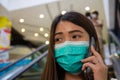 Asian woman wearing protective face masks against air pollution PM2.5, prevent Coronavirus and talking on phone in public mall. Royalty Free Stock Photo