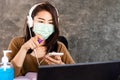 Asian woman wearing protective mask spraying alcohol cleaning screen of smart phone for anti covid-19 virus at work
