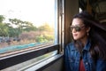 Asian woman wearing sunglasses travel by train sitting near the window and looking through the train window.