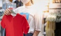 Asian woman wearing surgical mask and choosing the red t-shirt clothes and looking to mirror in mall or clothing store Royalty Free Stock Photo