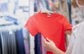 Asian woman wearing surgical mask and choosing the red t-shirt clothes and looking to mirror in mall or clothing store Royalty Free Stock Photo