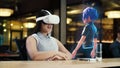 Asian woman wearing VR headset communicates with cartoon character via hologram