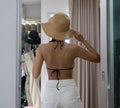 An Asian woman wearing white jeans is trying out a bikini and straw hat in her bedroom for a beach holiday