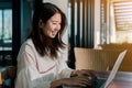 Asian woman Wearing a white shirt sitting in front of a laptop computer With a happy smile