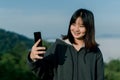 Asian woman Wearing a winter jacket, take a selfie phone, take pictures in the tourist area behind the fog and mountains with a Royalty Free Stock Photo