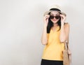 Asian woman  wearing yellow sleeveless shirt and hat, holding woven bag, standing on white background, taking off sunglasses, Royalty Free Stock Photo