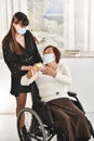 Asian woman in a wheelchair giving a golden wrapped gift box to a young woman behind her