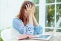 An Asian woman in a white shirt sits in a bakery, clutching her head in stress with her purse and laptop next to it Royalty Free Stock Photo