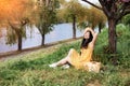 Asian woman in a wicker hat in city park. Portrait of a stylish model in a yellow dress near pink flowering trees.