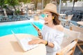 Asian woman wirking with mobile phone and laptop pc and relaxing near swimming pool. Distant work concept Royalty Free Stock Photo