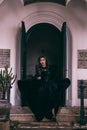 an Asian woman with a witch-like appearance flung her all-black skirt in the air as she stood in front of a cemetery