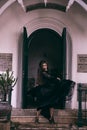 an Asian woman with a witch-like appearance flung her all-black skirt in the air as she stood in front of a cemetery