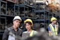 Asian woman worker with safety vest and helmet holds tablet, reports information to her supervisor senior foreman at manufacturing Royalty Free Stock Photo