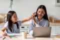 Asian woman working on laptop computer from home while daughter distracting her, taking off mom's glasses Royalty Free Stock Photo