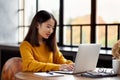 Asian woman working on laptop at home or in cafe. Young lady in bright yellow jumper