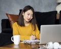 Asian woman working on laptop at home or in hotel. Young lady in bright yellow jumper