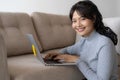 Asian woman is working on a laptop in  living room. She sit on the floor and sofa is office desk. On her face are smile and Royalty Free Stock Photo