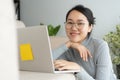 Asian woman is working on a laptop in the living room. She sit on the floor and sofa is office desk. On her face are smile and Royalty Free Stock Photo