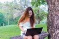 Asian woman working on a laptop smiling at a garden or park