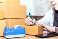 Asian woman writing address on box. Young asian woman entrepreneur, woman wrapping boxes to send via mail online business concept Royalty Free Stock Photo