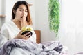 Asian woman yawning in bed hand holding alarm clock feeling tired and sleepy