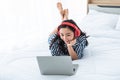 Asian woman, 23 years old, Wears red headphones She smiles happily while using a notebook computer On her white bed Royalty Free Stock Photo