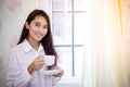 Asian women drinking coffee and wake up in her bed fully rested and open the curtains in the morning to get fresh air on sunshine Royalty Free Stock Photo