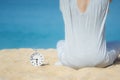 Asian women in a gray dress sitting beside the white alarm clock placed on the sand. Blue sea and sky as a background. Concept for Royalty Free Stock Photo