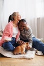 Joyful asian woman holding coffee and hugging african american boyfriend with pet at home Royalty Free Stock Photo