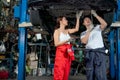 Asian woman mechanic help her co-worker man to fix the problem of car in area under the car and the work in workplace of garage