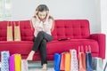 Asian women sit on a red sofa and feel stressed, sad and depressed expression with a lot of colorful shopping paper bags,Concept