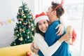 Asian woman with surprise Christmas gift hugging husband at home. Presenting gift as Christmas eve tradition, celebrating New Year