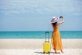 Asian women traveler holding yellow luggage walking and take a photo smart phone on the beach.