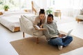 Asian woman in warm clothes reading book near african american boyfriend using laptop in bedroom at home Royalty Free Stock Photo