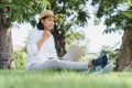 Asian women wear hat are using laptop with wired headphones while sitting on grass green  In the public park Royalty Free Stock Photo