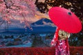 Asian women wear Japanese kimonos. Holding a red umbrella at Mount Fuji and cherry blossoms in Japan Royalty Free Stock Photo