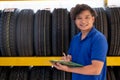 Asian worker or employee of auto parts shop hold the document and stand in front of tires on shelves and look to camera with