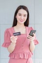 Asian working woman who wears pink dress holds smartphone and credit card in her hands in finance choice theme Royalty Free Stock Photo