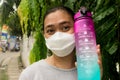 Asian workout woman wearing face mask holding drinking water bottle