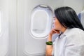 Asian wowan rest hand on chin in airplane cabin near window seat