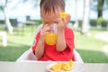 Asian 1 year old toddler baby boy child sitting in high chair holding & drinking tasty orange juice Royalty Free Stock Photo