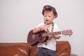 Asian 2 - 3 years old toddler baby boy child wearing hat hold & play Hawaiian guitar or ukulele in living room at home Royalty Free Stock Photo