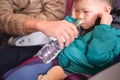 Asian 2 - 3 years old toddler boy child holding his aching ear and drinking water from bottle during flight on airplane. Little