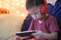 Asian 2 -3 years old toddler boy child listening to music with headphones from smartphone, Kids playing with phone in bedroom at h