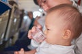 Asian 2 years old toddler boy child suffering from aching ear drinking water from bottle during flight on airplane. Little kid