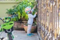 Asian 2 - 3 years old toddler boy child wearing safety helmet near his bike, Kid reaching up try to open gate of the house Royalty Free Stock Photo